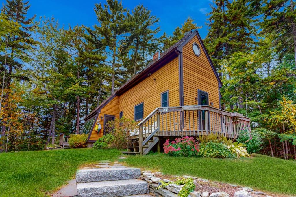 a home with a large wooden house with a porch at Appalachee Pond Waterfront Cottage | Decks, Sunroom, Dock with Kayaks & Canoe in Boothbay Harbor