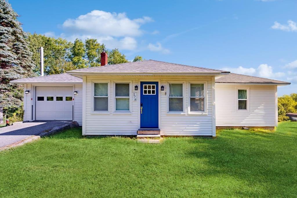 a white house with a blue door in a yard at Charming Cottage with Cozy Comfort and Easy Access to Outdoor Adventures in North Lamoine