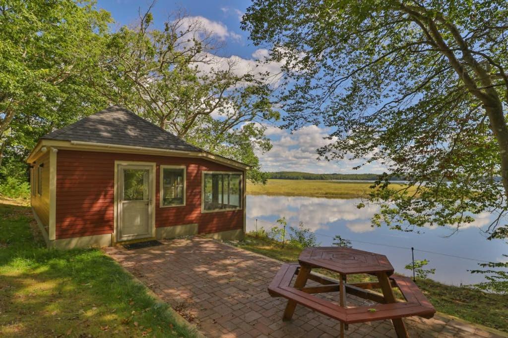 a tiny house with a picnic table next to a lake at Luxe Bayfront Cabin w/ Stunning Views & Shared Dock- Ideal for Hunting & Fishing in Bowdoinham