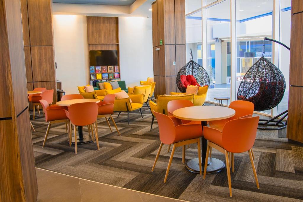 a restaurant with orange chairs and tables and windows at Tru By Hilton Puebla Angelopolis in Puebla