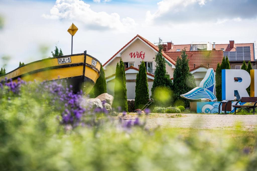 a boat in front of a building with purple flowers at Dom Gościnny Wiki in Rewal