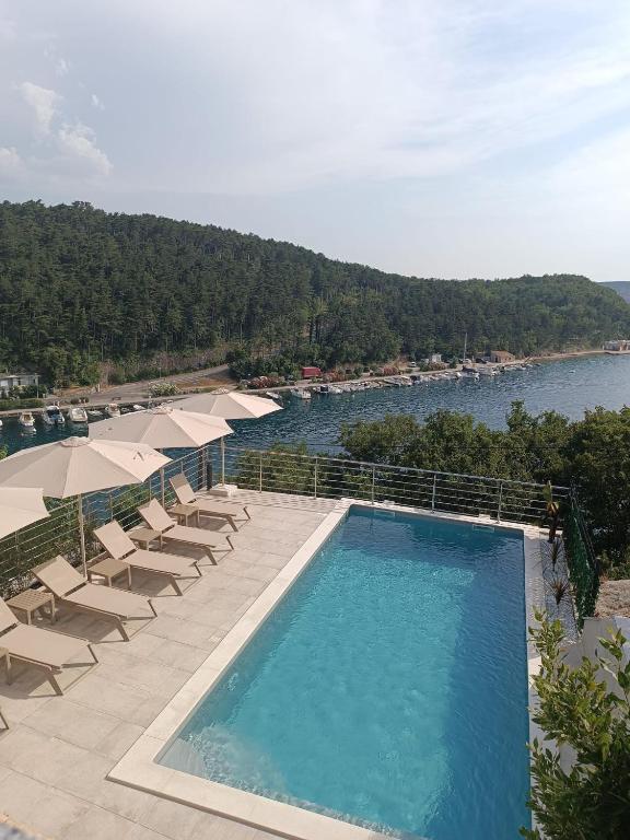 a swimming pool with chairs and umbrellas and a body of water at Dream View Villa in Jadranovo