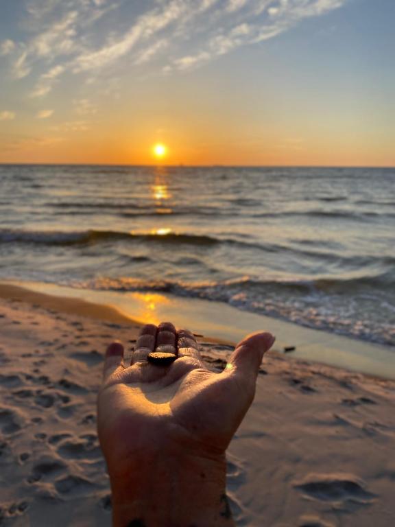a persons hand is reaching for the sunset on the beach at Sunny House Baltic in Kopalino