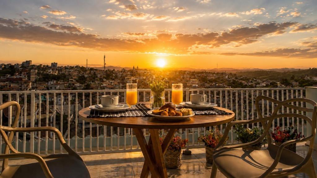 a table with a plate of food on a balcony with the sunset at Pousada Vista Chic in Cunha