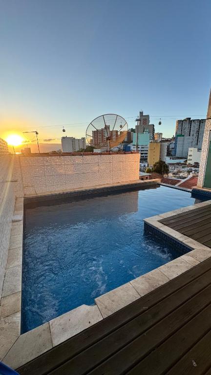 a swimming pool with the sun setting in a city at Apartamento com piscina privativa 7 minutos da basílica in Aparecida