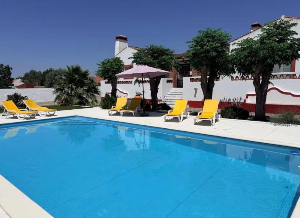a large swimming pool with yellow lounge chairs and a building at Tapada Poço das Canas in Redondo