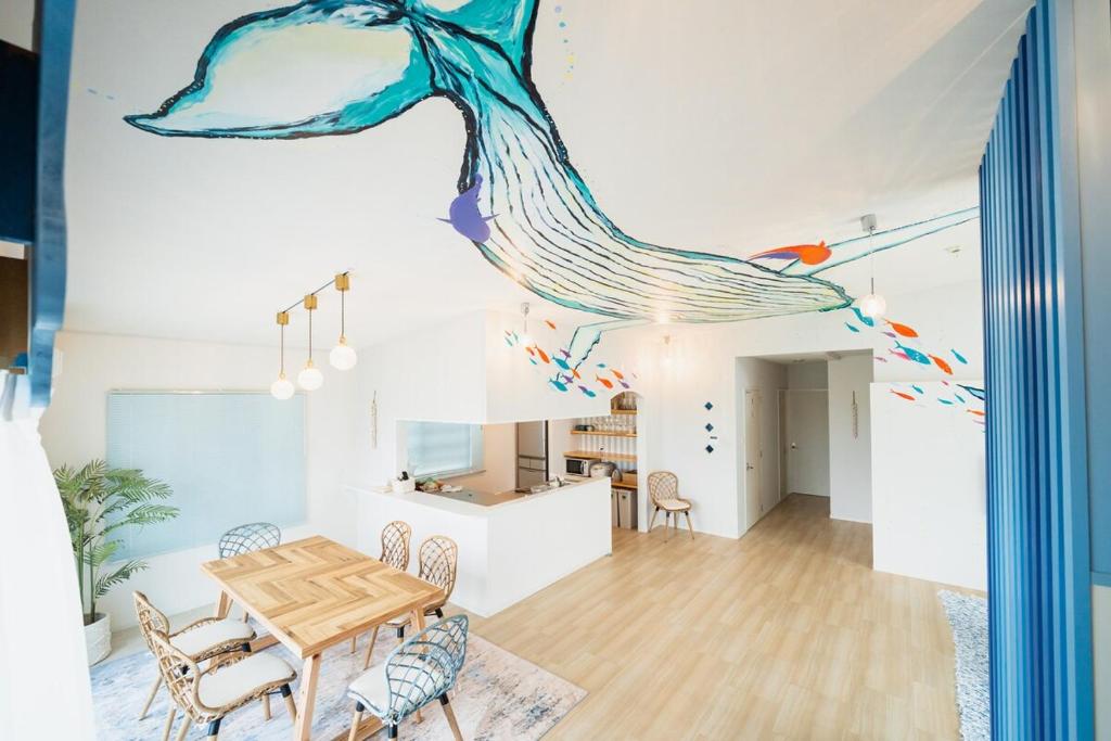 a dining room with a table and a peacock painting on the wall at The Mural Art House Bise in Motobu