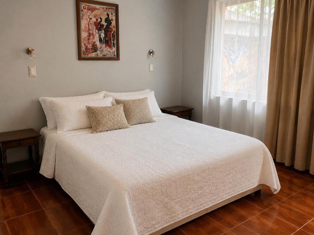 a bedroom with a white bed with pillows and a window at NEW Hotel Casa del Profesor in Iquique