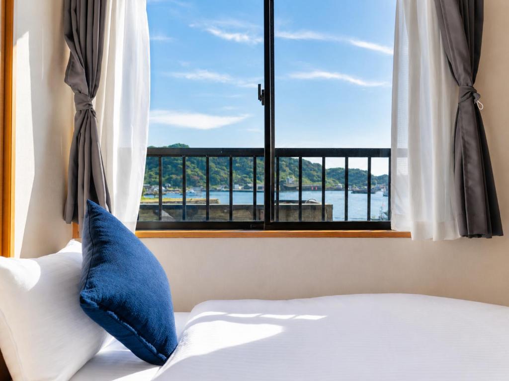 a bed with a blue pillow in front of a window at Good Stay Apartment Nichinan - Sea View & Free Parking in Nichinan