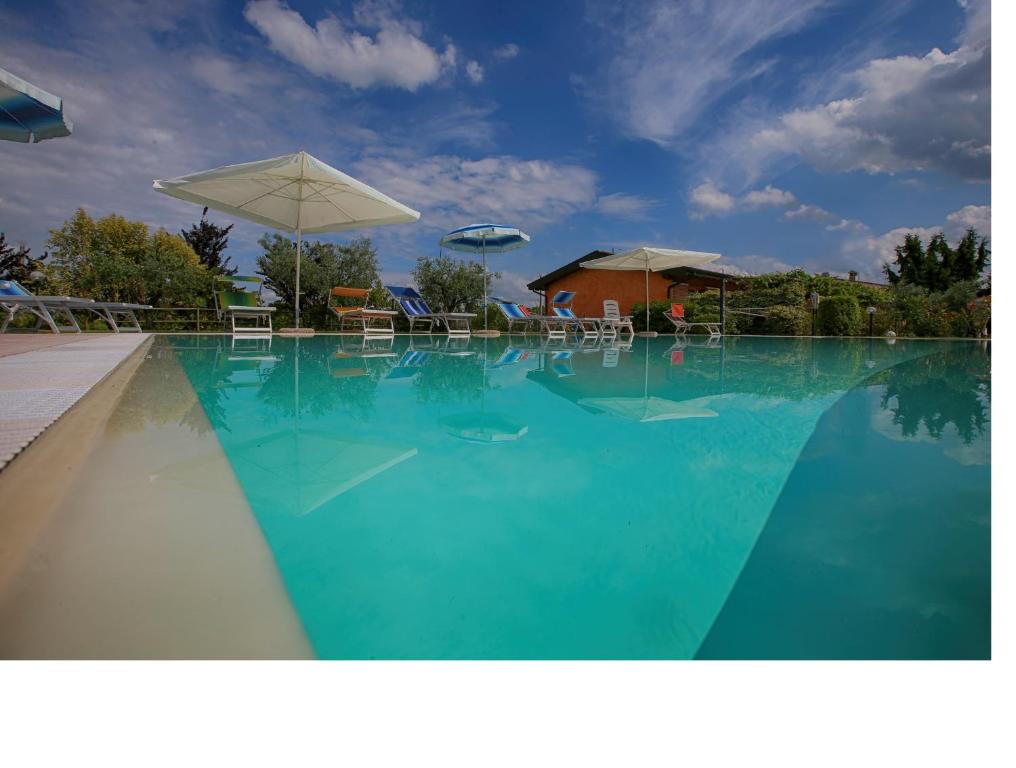 una grande piscina con acqua blu e ombrelloni di Agriturismo La Palazzina a Castelnuovo del Garda