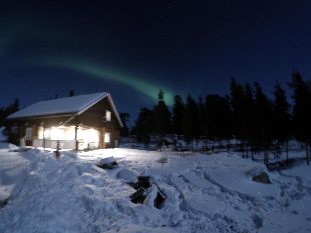 una cabaña en la nieve por la noche con luz verde en Inari Juutua, en Inari