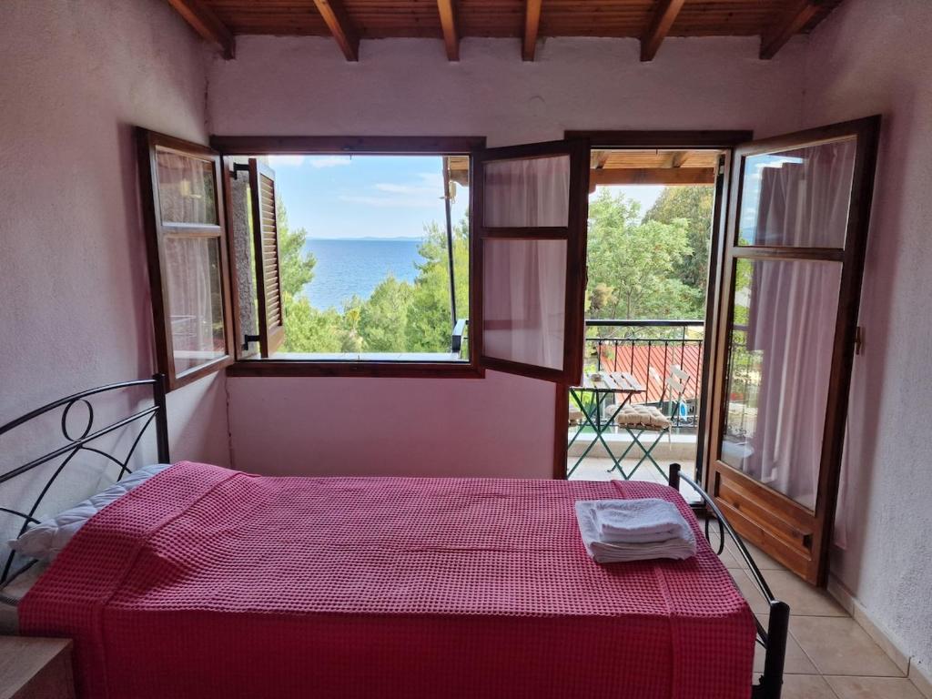 a bedroom with a bed with a red comforter and two windows at Cozy apartment with a great view! R in Metamorfosi