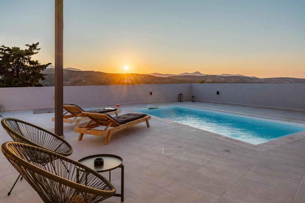 a patio with a pool and chairs and the sunset at Villa Esperia in Áyios Síllas