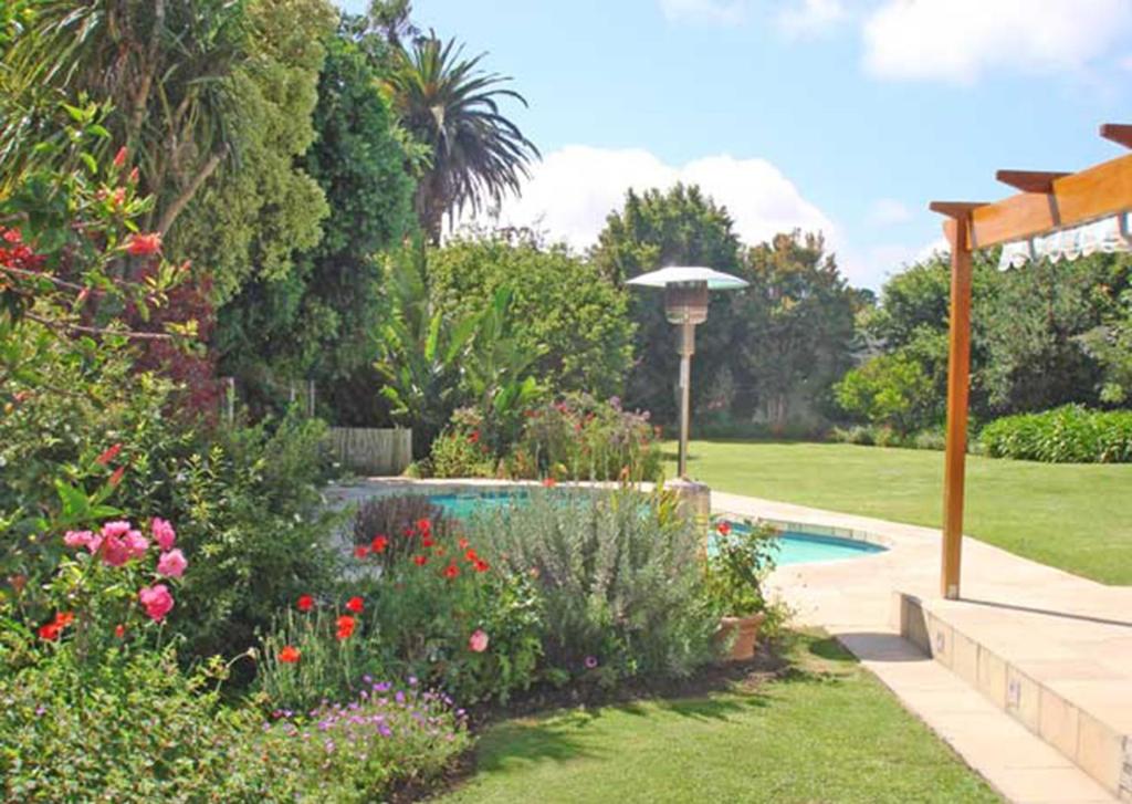 a garden with a swimming pool with flowers and an umbrella at Francolin's Rest Guest Suite in Sweet Valley