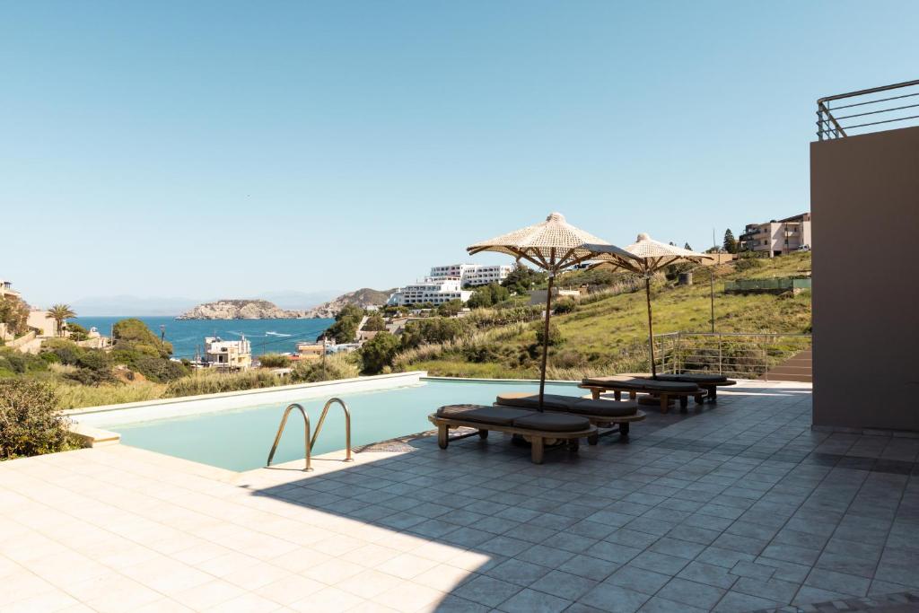 a pool with two benches and an umbrella and the ocean at Villa Mononaftis in Agia Pelagia