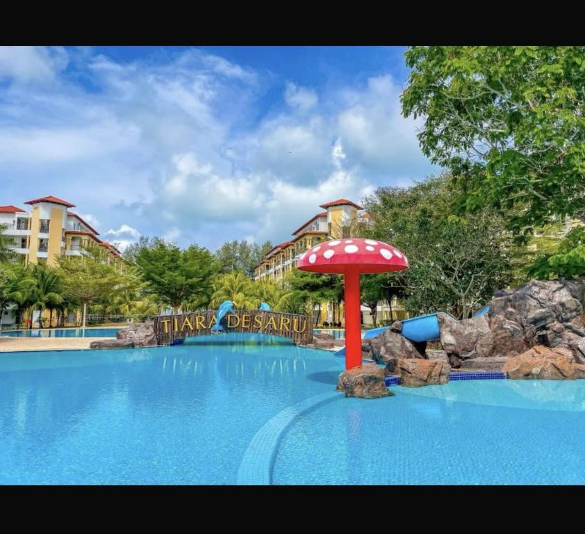 a pool at a resort with a red umbrella in the middle at Tiara Homestay Desaru - Garden Pool View in Bandar Penawar