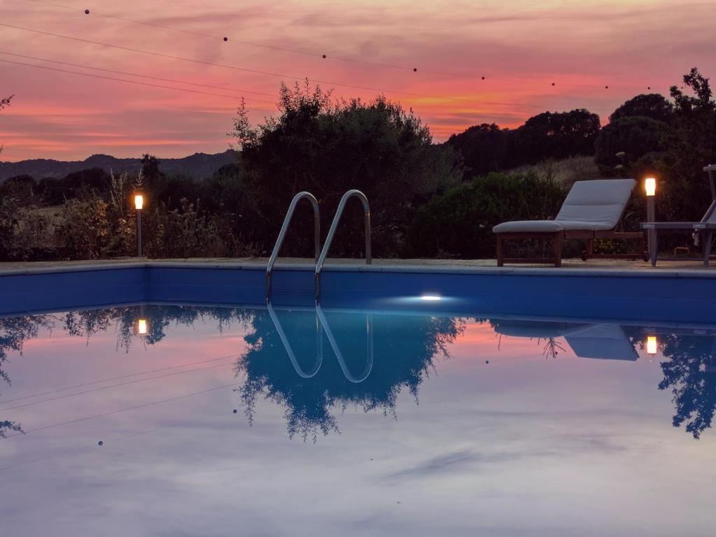 a swimming pool with a sunset in the background at Agreen Country House in Olbia