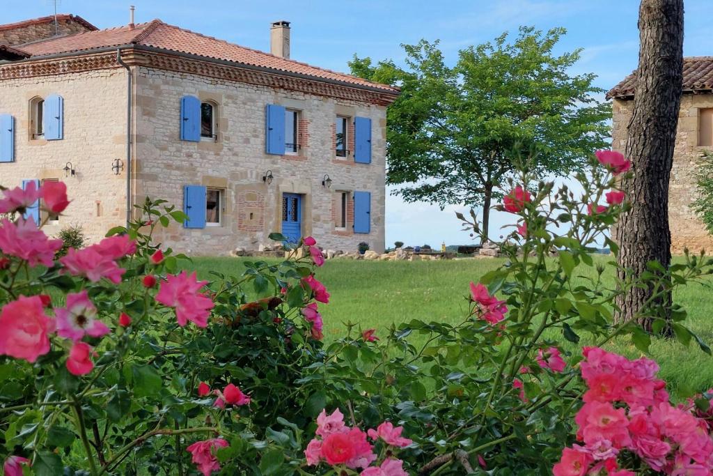 an old stone house with blue windows and pink flowers at Clos de la Dîme in Lombers