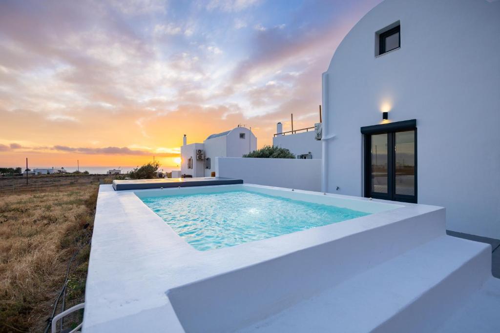 a white villa with a plunge pool in front of a sunset at Aerial Villas in Imerovigli
