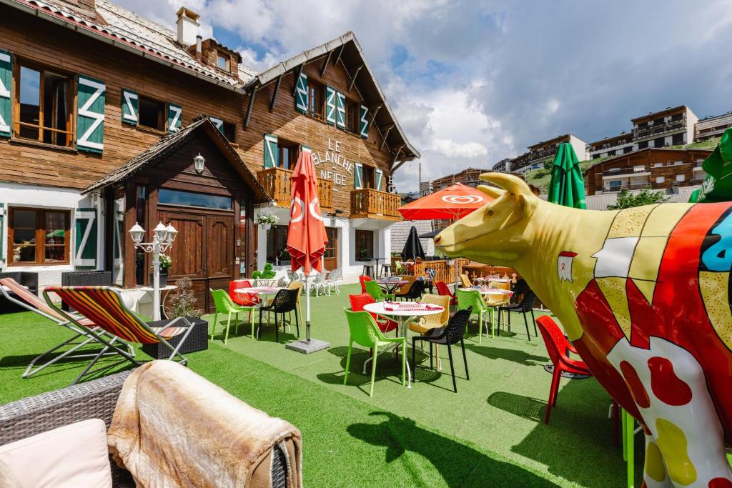 a patio with tables and chairs and a statue of a cow at Hotel Le Blanche Neige in Valberg