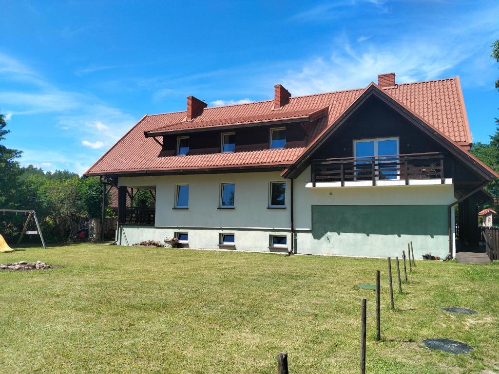 a house with a red roof and a yard at Biały Dom - Pokoje in Wejsuny