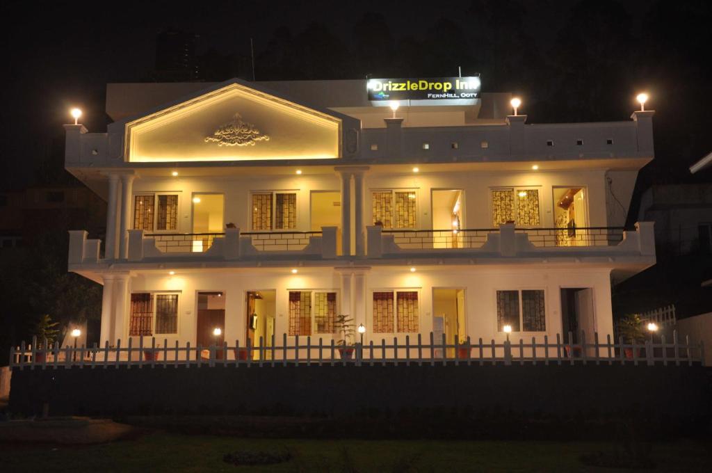 a large white building with a sign on top at night at Drizzle Drop Inn in Ooty