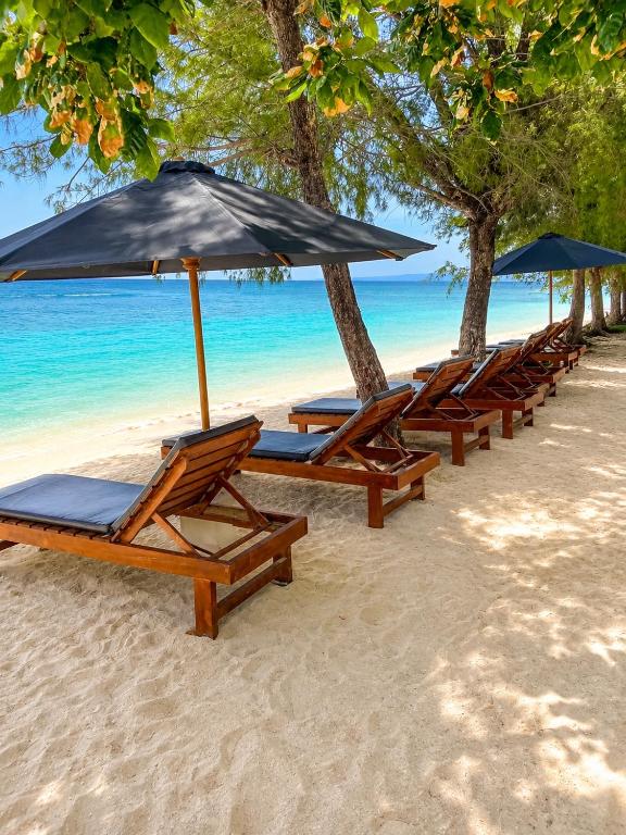 a row of lounge chairs and umbrellas on a beach at Villa Samalas Boutique Resort & Private Pool Villas in Gili Meno