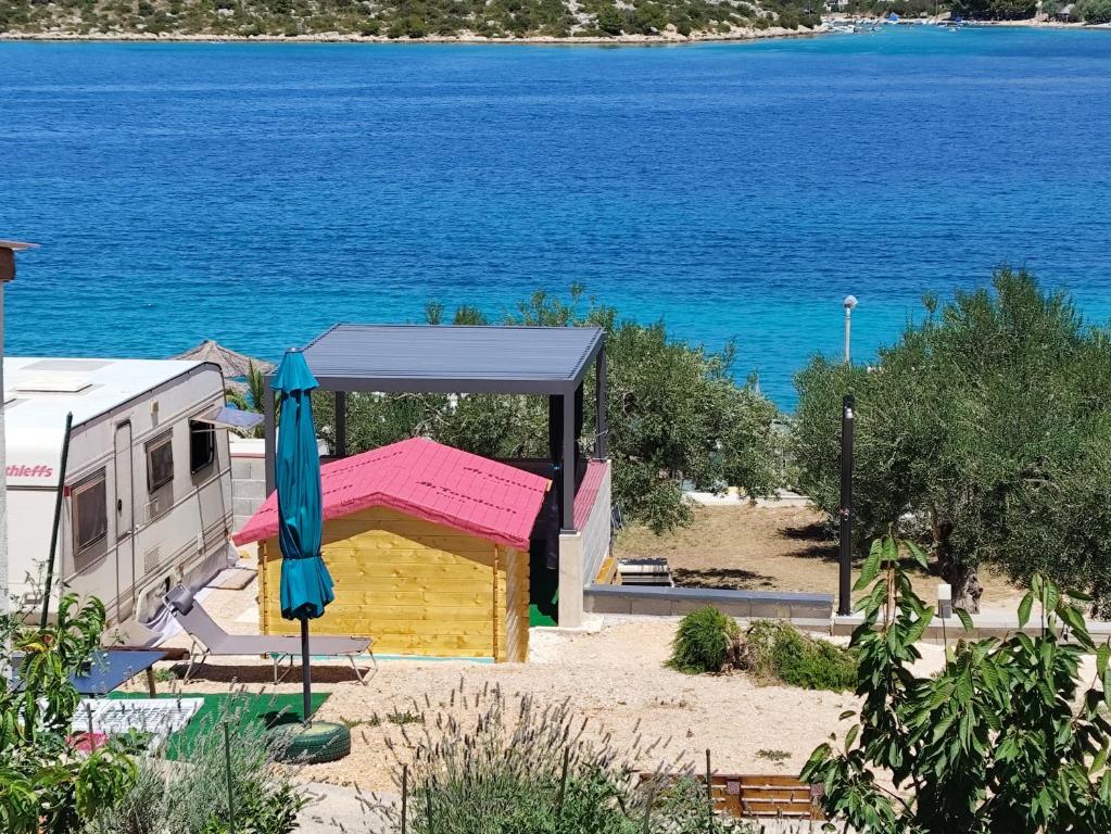 a building with an umbrella next to the water at Caravan with private toilet and kitchen 2 in Grebaštica