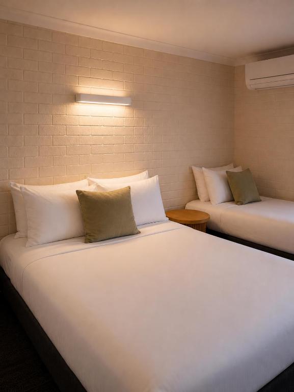a bedroom with two beds with white sheets and pillows at Busselton Motel in Busselton