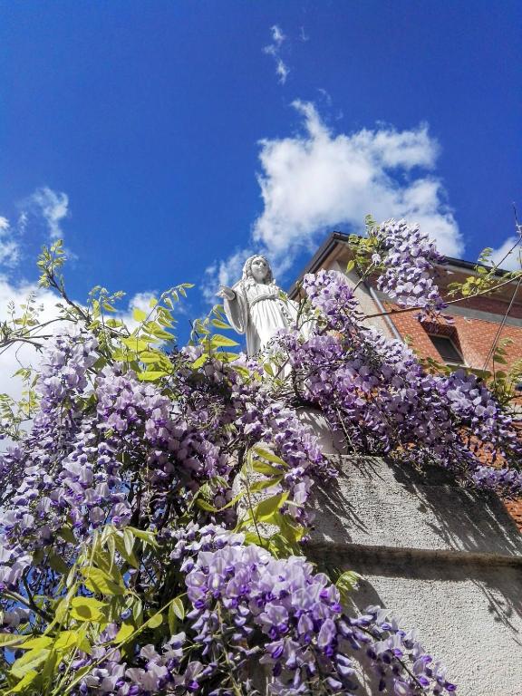 a statue behind a bunch of purple flowers at Oasi della Divina Volontà in San Giovanni Rotondo