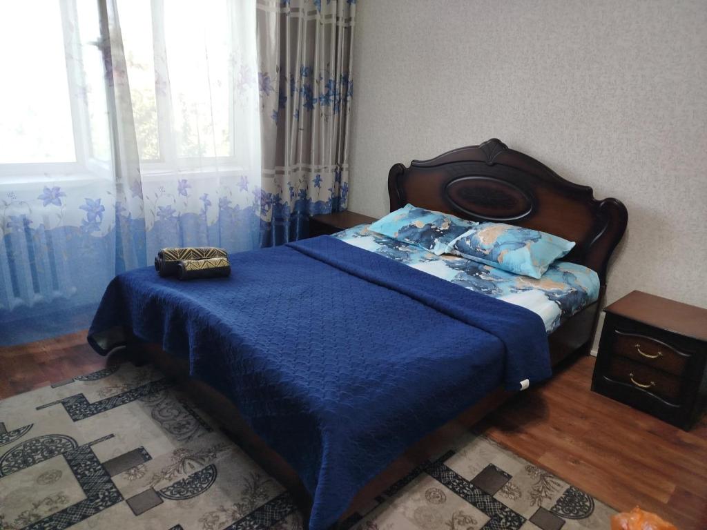 a bedroom with a bed with a blue blanket and a window at Квартира in Taraz