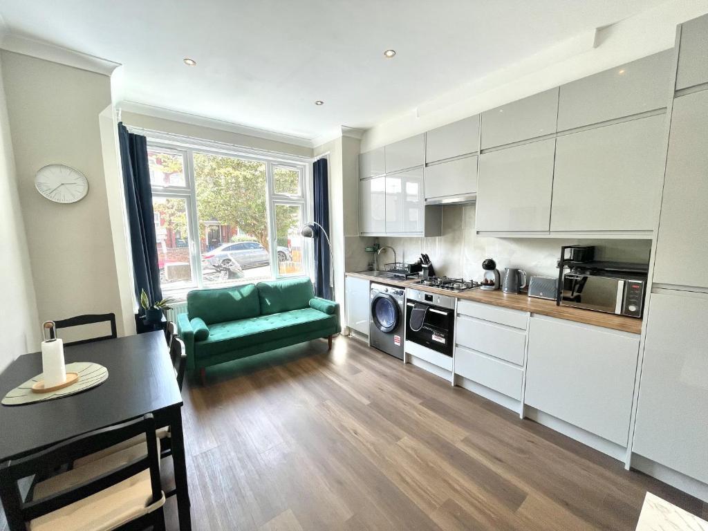 a kitchen with white cabinets and a green couch at Stylish 2BR Flat 3 Mins to Wembley Stadium in London
