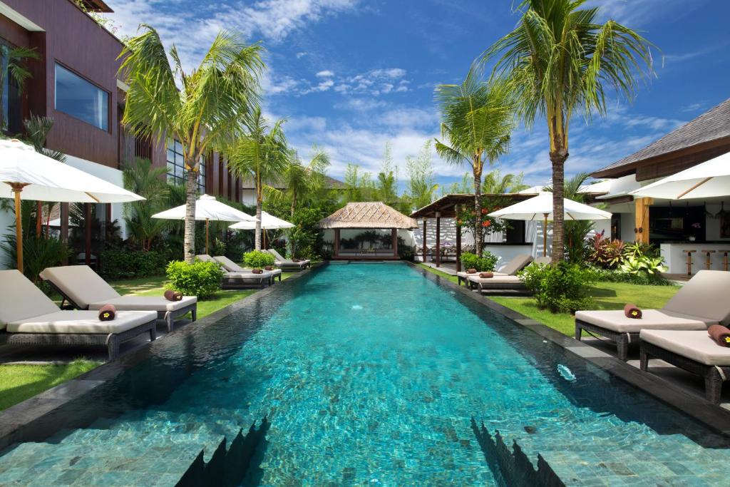 a pool at a resort with chairs and umbrellas at Villa Anam in Seminyak