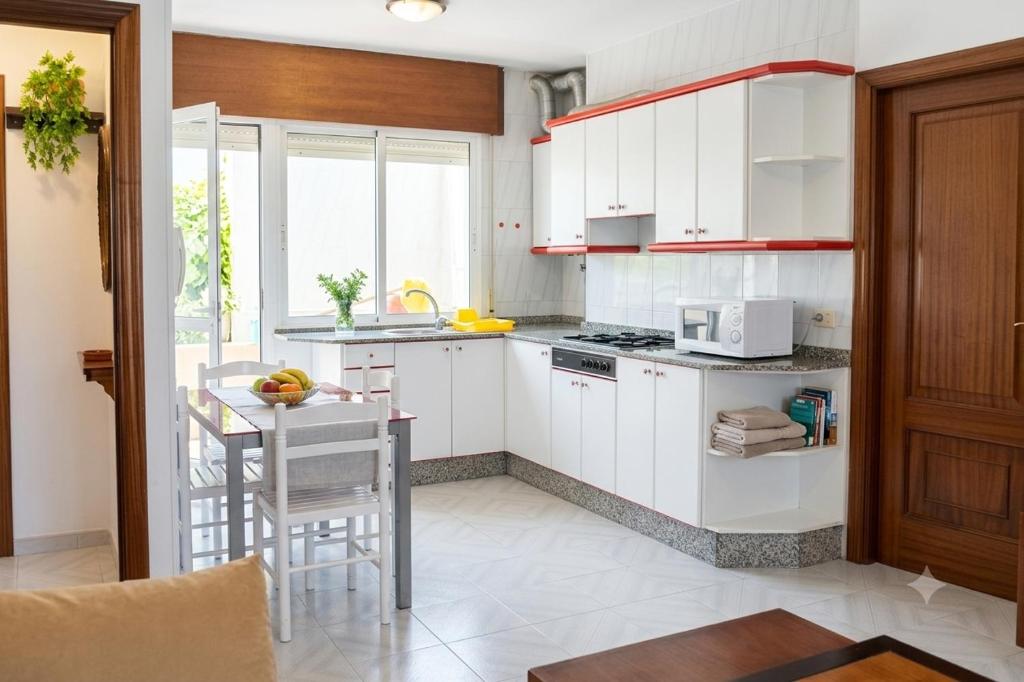a kitchen with white cabinets and a table with chairs at Céntrico Apartamento Rosalía 3H in O Grove