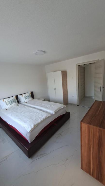 a white bedroom with a large bed and a wooden dresser at Apartman Ishar in Bihać