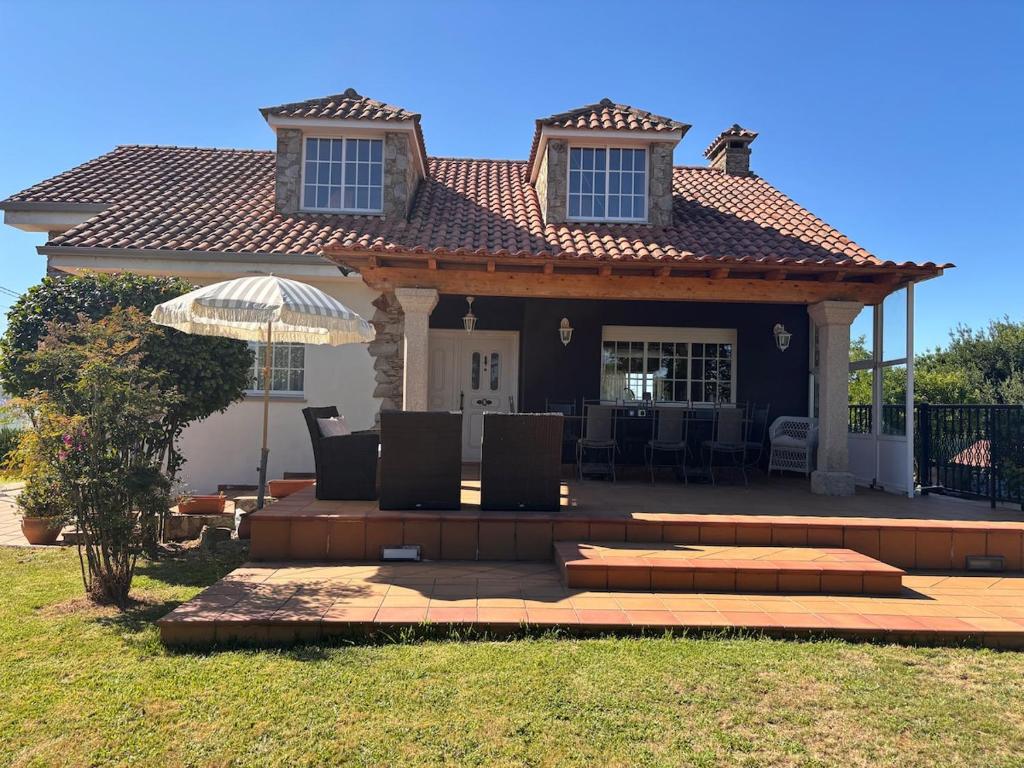 a house with a patio with chairs and an umbrella at Cumbre- chalet con piscina cubierta y vistas al mar en Sada in Sada