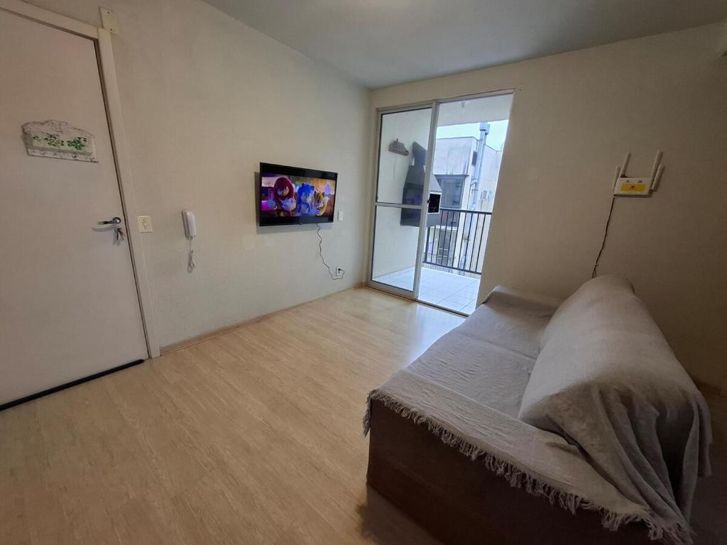 a bedroom with a bed and a door with a television at Apartamento com sacada, estacionamento e piscina in São Leopoldo