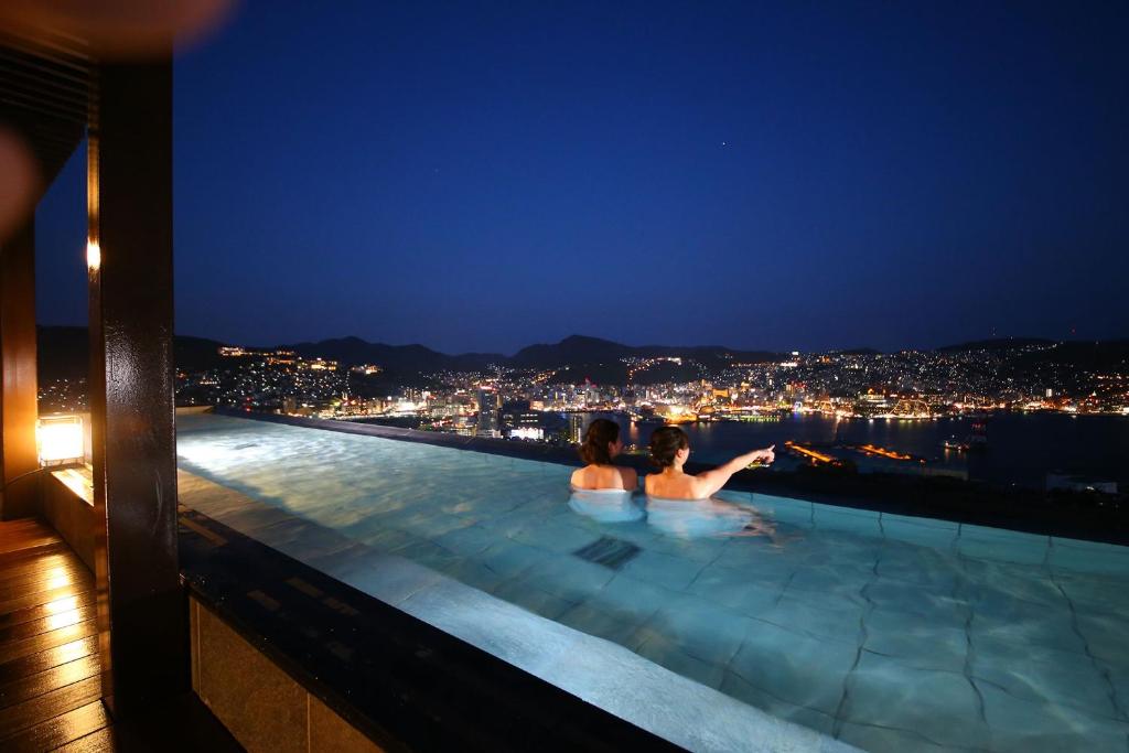 two people sitting in a infinity pool at night at Ooedo Onsen Monogatari Premium Nagasaki Hotel Seifu in Nagasaki
