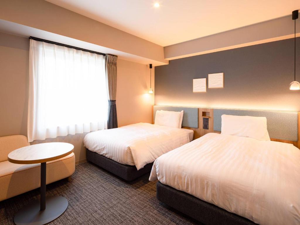 a hotel room with two beds and a table at Comfort Hotel ERA Sapporo North in Sapporo