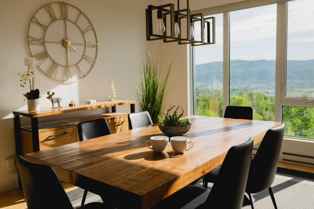 a dining room with a wooden table and a large clock at Elegant Condo - Balcony Pool & Stunning View in Baie-Saint-Paul