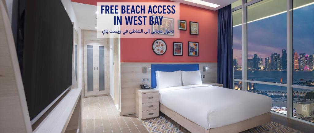 a bedroom with a white bed and a large window at Hampton By Hilton Doha Old Town in Doha