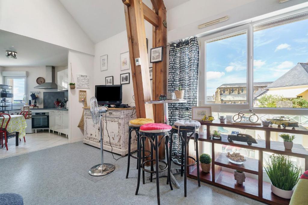 a living room with stools and a kitchen with windows at Joli Duplex Centre-ville 5km Dinard in Pleurtuit