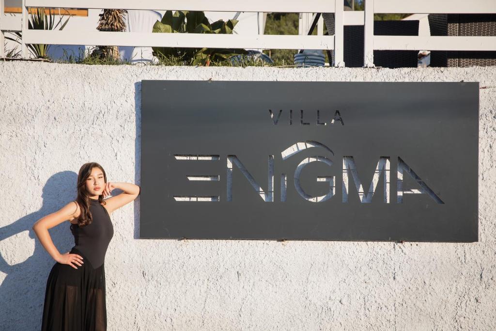 a woman in a black dress standing in front of a sign at Villa Enigma in Gevgelija