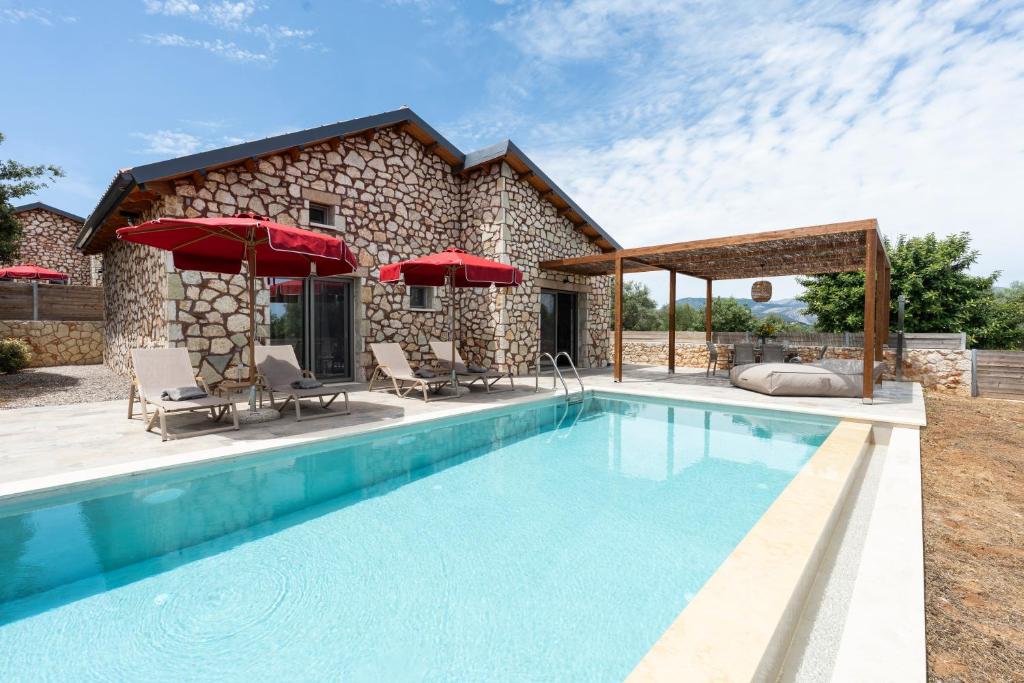 a swimming pool in front of a stone house with red umbrellas at Τilevoides Nisi Villas in Spartokhórion
