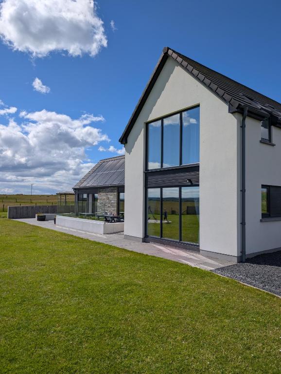 a white house with large windows and green grass at Flotnar Hús - Newbuild B&B in Keiss