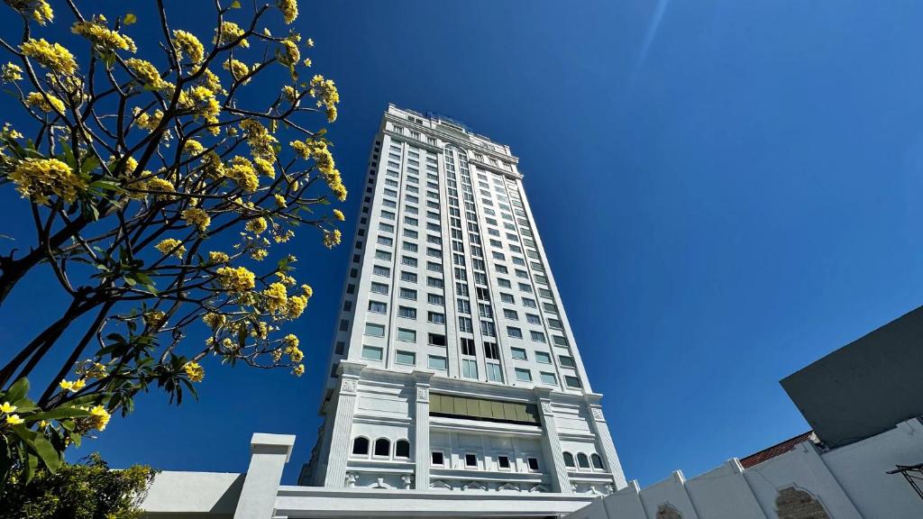 a tall white building with a tree in front of it at Rich Palace Hotel in Surabaya
