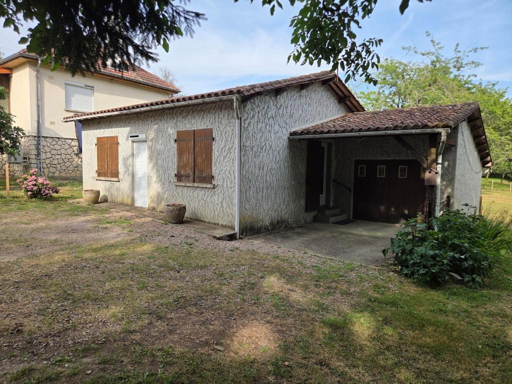 a small white building with a garage in a yard at Maison proche bourg in Piégut-Pluviers