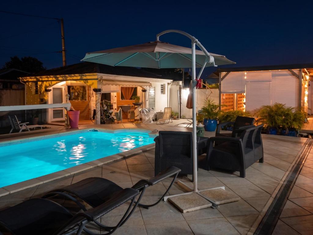 a swimming pool with chairs and an umbrella at Studio cosy aux Abymes, piscine et jardin, 25 m² in Les Abymes