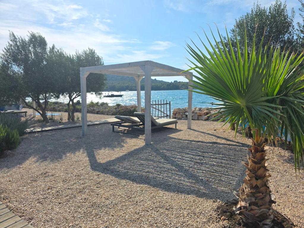a gazebo and a bench next to a palm tree at Villa Beach Charly in Tisno