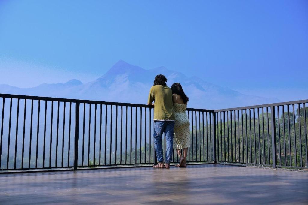 two people standing on a balcony looking at a mountain at Leal Resort-Wayanad in Meppādi